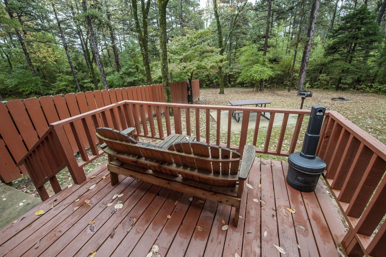 A view of the back deck with a seating area overlooking the outdoor space with picnic table and a grill at Cabin 1 at Crowley's Ridge State Park